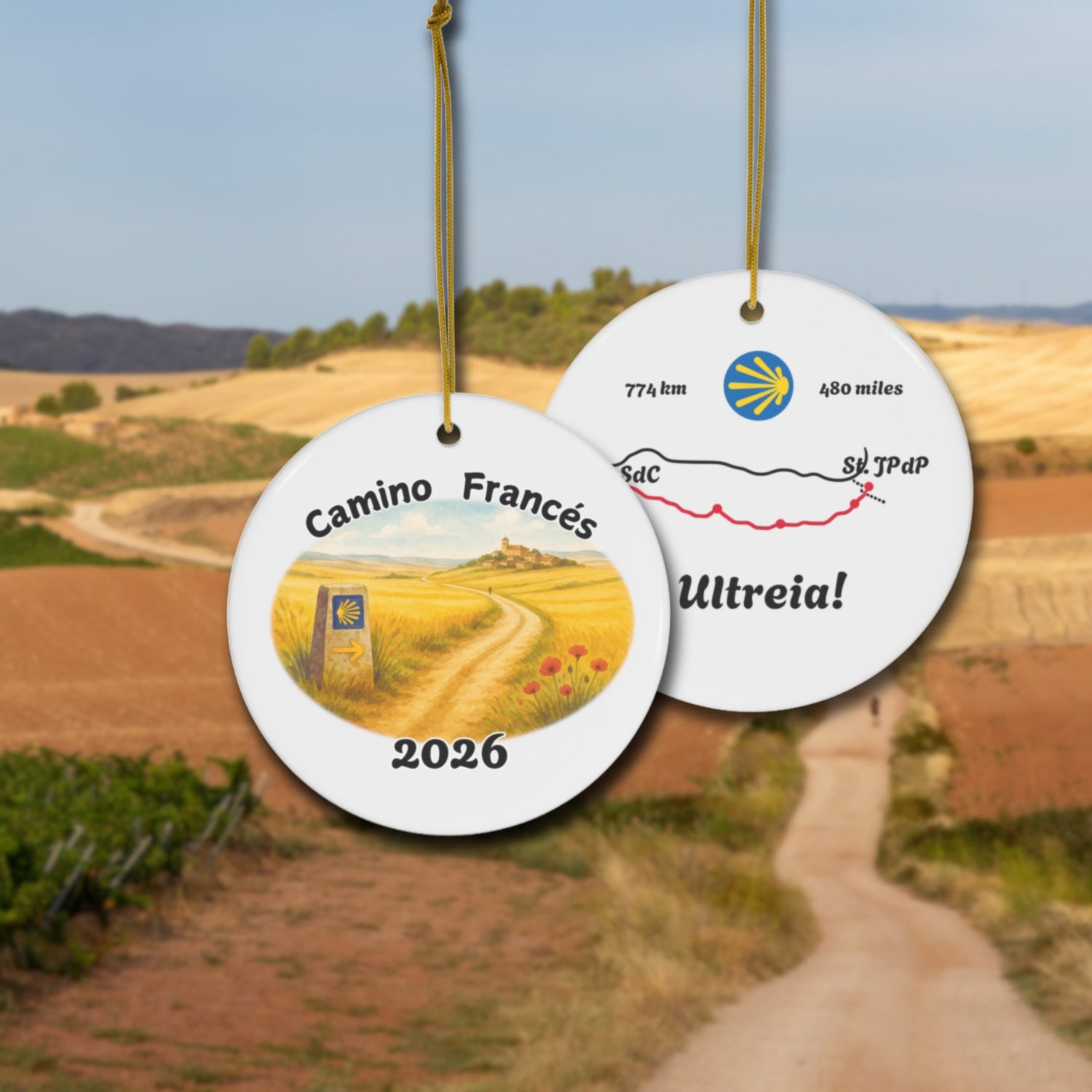 Camino Frances ceramic ornament with watercolor landscape shown front and back in front of trail landscape.
