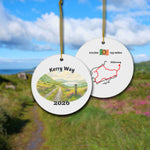 The Kerry Way ceramic ornament with watercolor landscape shown front and back in front of trail landscape.